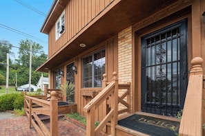 A wooden building with a porch, a black metal gate, and a brick pathway leading to the entrance.