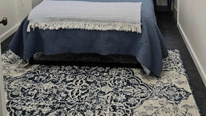 A bedroom with a bed, bedside lamps, a wall art piece, and a patterned rug.