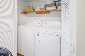 A laundry room with two washing machines, a shelf with cleaning supplies, and folded towels.