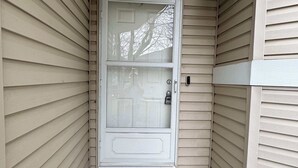 A house entrance with a white door, a black doormat, and a wall-mounted light fixture.