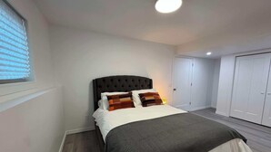 A bedroom with a large bed, a window with blinds, a ceiling light, and a wardrobe.