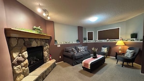 A living room with a stone fireplace, a sofa set, a coffee table, and a lamp.