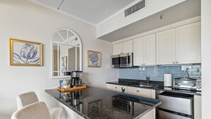 A compact kitchen with white cabinets, a black granite countertop, a microwave, a toaster, and a coffee maker. There are two framed floral artworks on the wall.