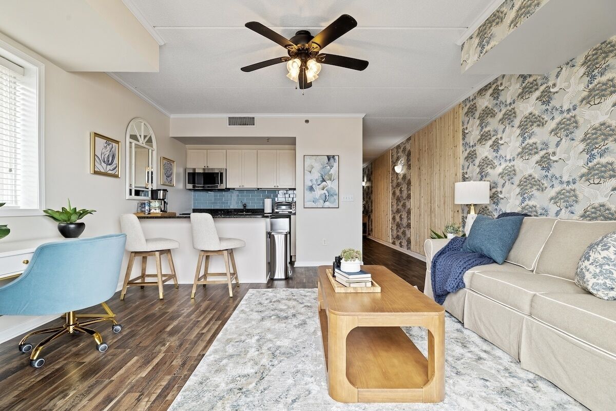 A modern living room with a ceiling fan, a coffee table, a sofa, and a kitchen in the background.