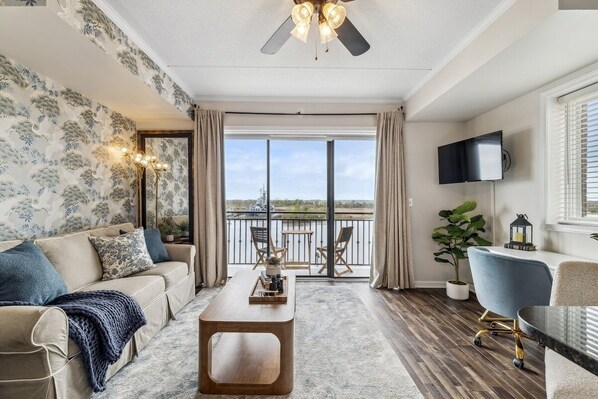 A spacious living room with a sofa, coffee table, and a balcony with a view. - Crane's Landing - Riverfront (Wilmington)