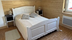 Ein Schlafzimmer mit Holzbalkendecke, einem weißen Bett mit zwei Kissen, einem Nachttisch mit Lampe und einem Fenster mit Blick auf einen roten Wagen.