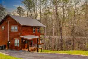 A two-story log cabin with a metal roof, a front porch, and a deck.