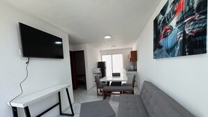 A living room with a sofa, a coffee table, a TV mounted on the wall, and a kitchen in the background. - Residencial Gran Cobae Dúplex A (Tonalá)