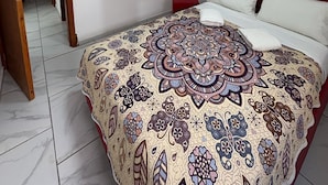 A bedroom with a large bed, a red headboard, a patterned bedspread, a white wall, a white shelf, and a door leading to another room. - Residencial Gran Cobae Dúplex A (Tonalá)