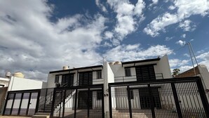 A two-story building with a white facade and black window shutters, surrounded by a black metal fence. - Residencial Gran Cobae Dúplex A (Tonalá)
