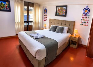 A hotel room with a large bed, two bedside tables with lamps, a window with curtains, and artwork on the walls. - WAYNA BOUTIQUE HOTEL (Cusco)
