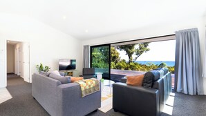 A modern living room with a grey sofa, a black sofa, a flat-screen TV, and a large window with a view of the ocean. - Glass Horizon - Rutherglen Holiday Home (Ruthherglen)