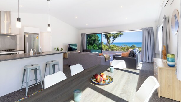A modern kitchen with a dining area, a sofa set, and a view of the sea. - Glass Horizon - Rutherglen Holiday Home (Ruthherglen)