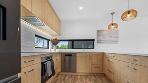A modern kitchen with wooden cabinets, a stainless steel dishwasher, and a window with a view of greenery.