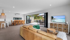 A modern living room with a large sofa, a dining area, and a TV displaying a beach scene.