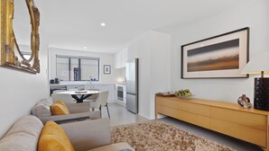 A modern living room with a sofa, a coffee table, and a wooden sideboard. There is a large window and a framed picture on the wall. - Modern Central Apartment - Christchurch Apartment (Christchurch)