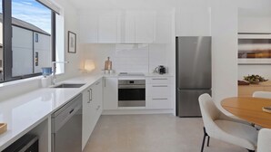 A modern kitchen with white cabinetry, stainless steel appliances, a built-in oven, and a dining area with a wooden table and chairs. - Modern Central Apartment - Christchurch Apartment (Christchurch)