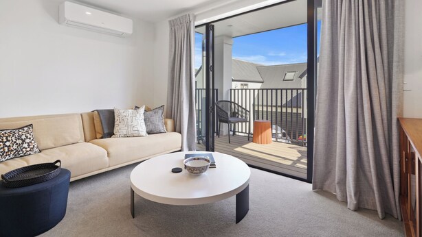 A modern living room with a sofa, a coffee table, and a balcony with a view. - Modern Central Apartment - Christchurch Apartment (Christchurch)