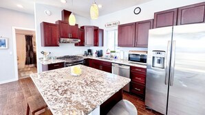 A modern kitchen with dark wood cabinets, stainless steel appliances, and a marble island. - 3-Bedroom House in Tranquil Homer, Alaska. Perfect Family Retreat. (Homer)