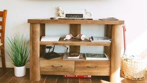 A wooden console table with a mounted TV, a sign with a wifi password, books, and a Monopoly game box. - 3-Bedroom House in Tranquil Homer, Alaska. Perfect Family Retreat. (Homer)