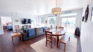 A spacious living area with a dining table, sofa, and a television mounted on the wall. - 3-Bedroom House in Tranquil Homer, Alaska. Perfect Family Retreat. (Homer)