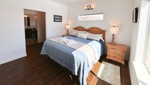 A bedroom with a bed, bedside lamps, a wooden nightstand, a window, and a door leading to a bathroom. - 3-Bedroom House in Tranquil Homer, Alaska. Perfect Family Retreat. (Homer)