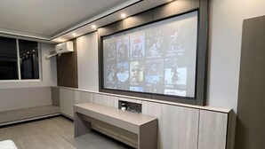 A modern hotel room with a large wall-mounted TV displaying various images, a built-in bench, and a window with curtains. - Juya Business Hotel (Shanghai)