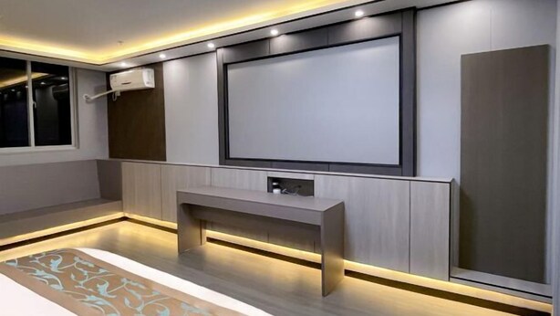 A modern room with a large flat-screen TV mounted on the wall, a built-in bench, and recessed lighting. - Juya Business Hotel (Shanghai)