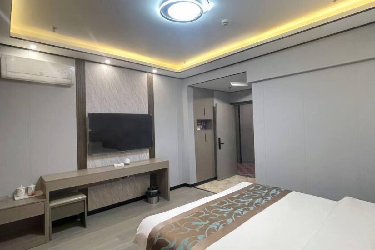 A modern hotel room with a bed, a desk, a mirror, and a wardrobe.