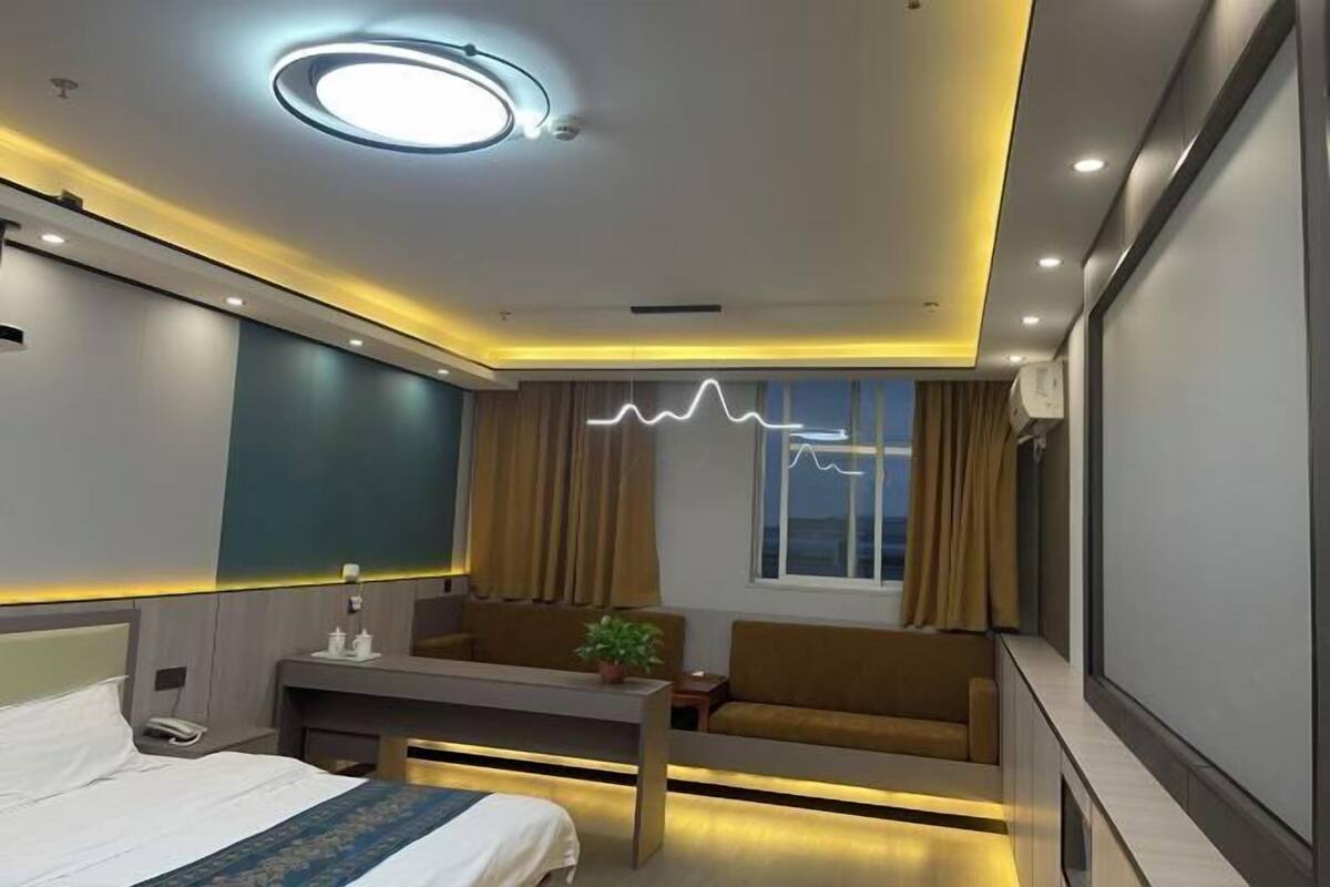 A modern hotel room with a bed, a desk, a sofa, and a large window.