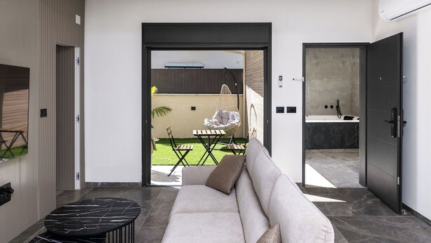 A modern interior with a sofa, a small table, and a chair in a well-lit space with a view to an outdoor area.