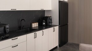A modern kitchen with white cabinets, a black countertop, and a black refrigerator.