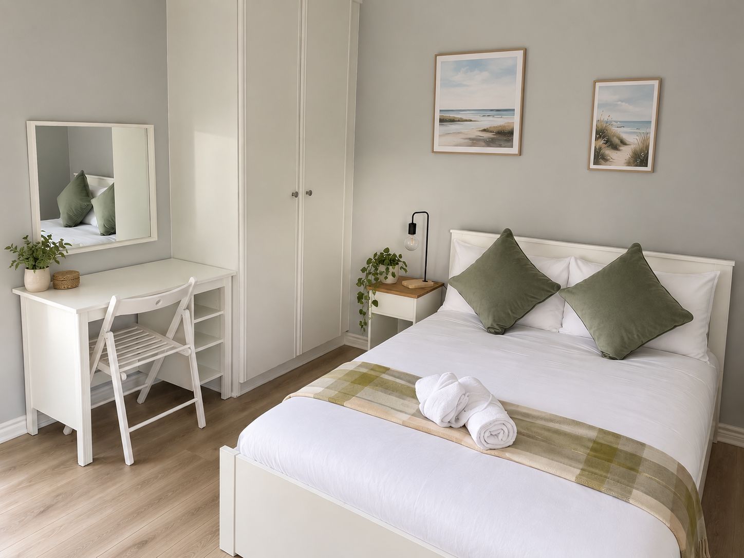 A bedroom with a bed, a desk, a chair, a nightstand, and two framed pictures on the wall.