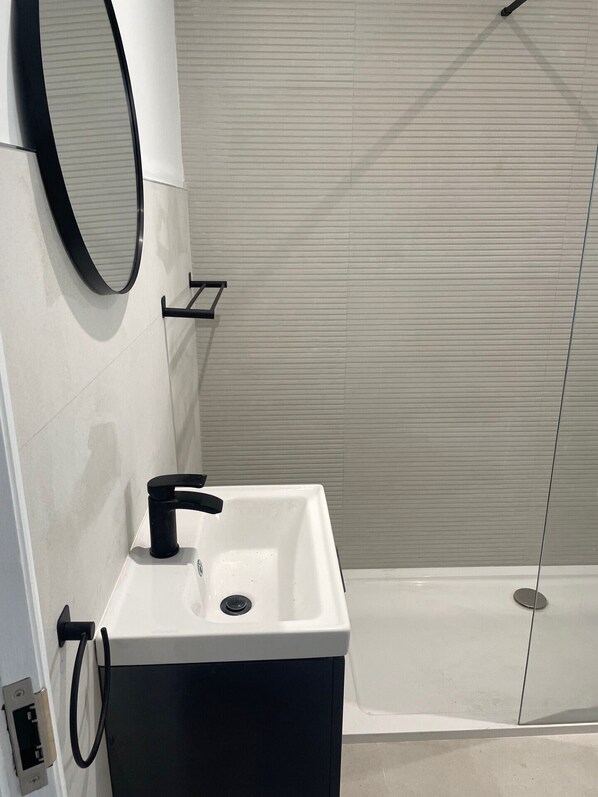 Un baño moderno con lavamanos blanco, grifo negro y un espejo.