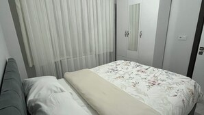 Ein Schlafzimmer mit einem Bett, einem grauen Sofa, einem Kleiderschrank und einem Spiegel.