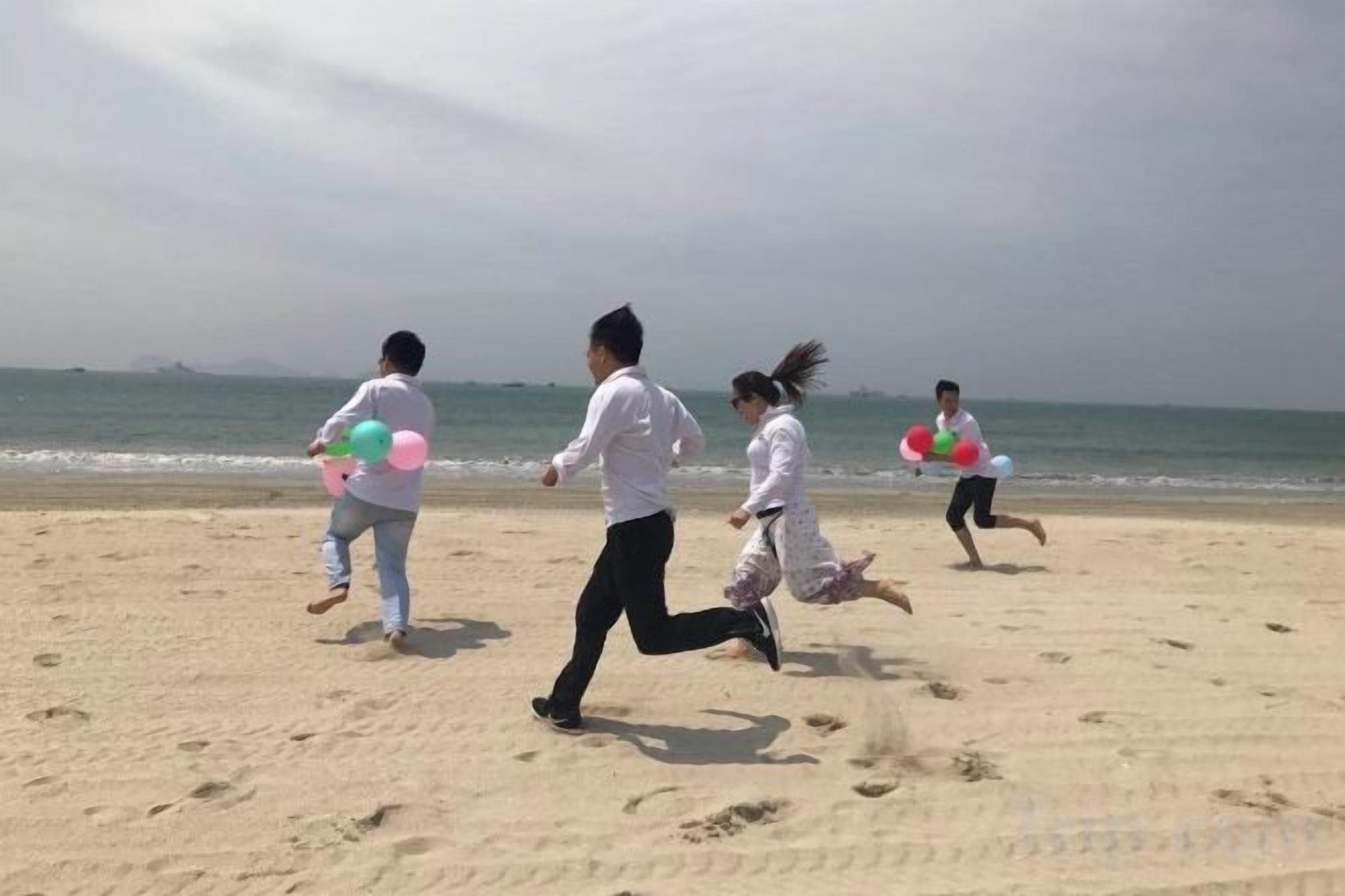 A beach scene with people running and holding balloons.