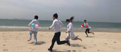 A beach scene with people running and holding balloons.