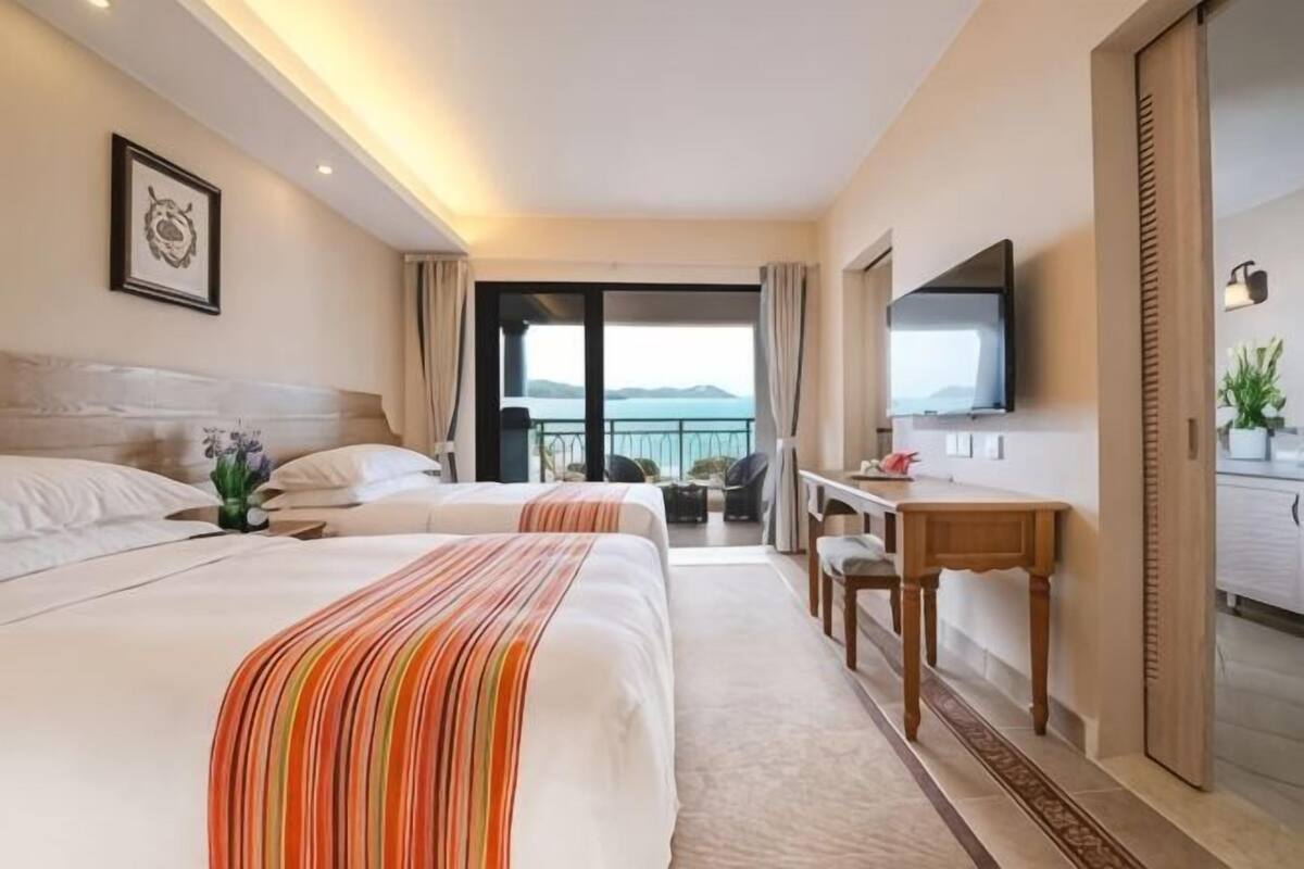 Ein Hotelzimmer mit zwei Betten, einem Schreibtisch, einem Fernseher und einem Balkon mit Blick.