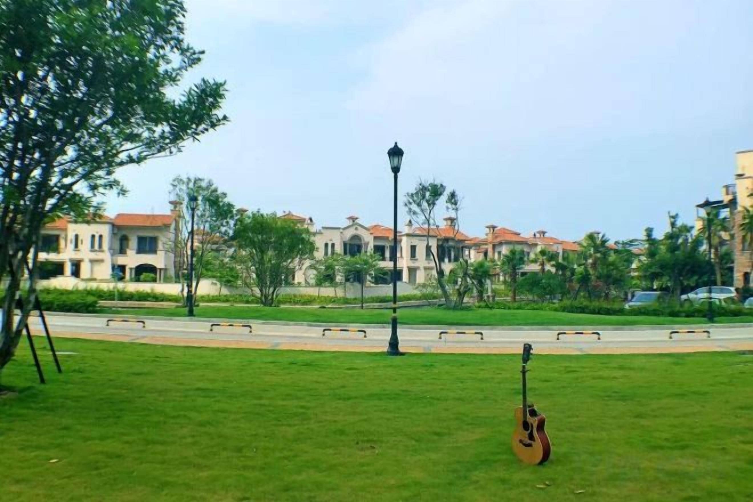 Zona verde con una guitarra, un farol y una calle con edificios al fondo.