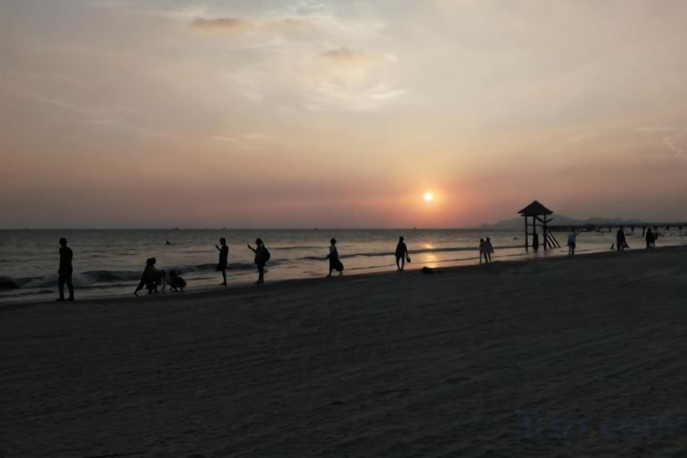 A beach scene with people walking along the shore during sunset.