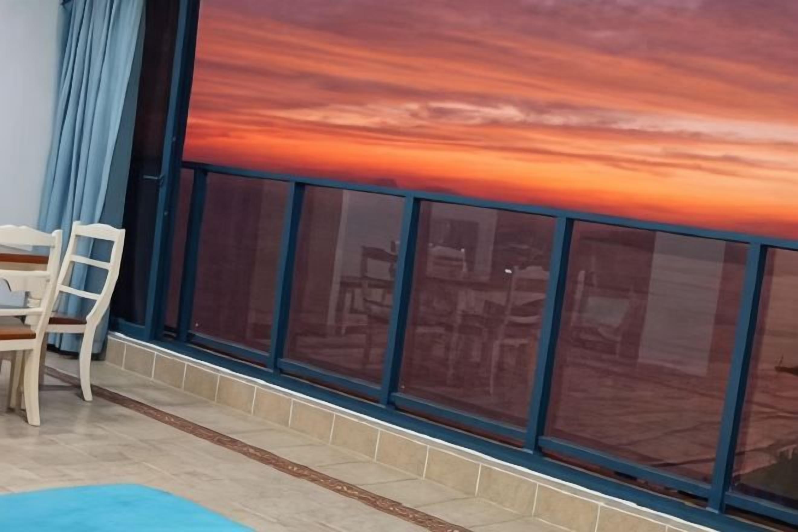 Una habitación con un amplio ventanal, una mesa de comedor con sillas y una alfombra azul.