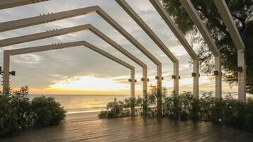 Una terraza de madera con estructura de pérgola, con vistas a una masa de agua durante el atardecer.