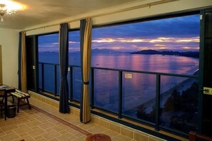 Een kamer met een groot raam dat uitkijkt op een waterpartij, een eethoek met stoelen en een betegelde vloer.