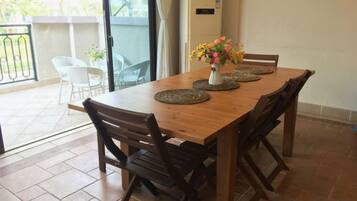 A wooden dining table with four chairs, a vase with flowers, and a view of a balcony with chairs.