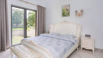 Ein Schlafzimmer mit einem großen Bett, einer Bank, einem Nachttisch und Blick durch eine Schiebetür ins Freie.