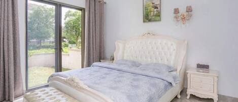 A bedroom with a large bed, a bench, a nightstand, and a view through a sliding door to the outdoors.