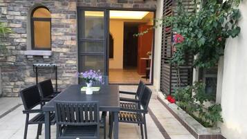 Un patio exterior con una mesa y sillas, un muro de piedra y un gran ventanal corredizo que da a un espacio interior.