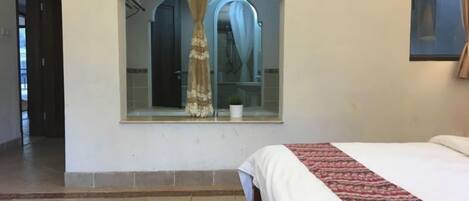 A hotel room with a bed, a large window with a curtain, a mirror, and a rug.