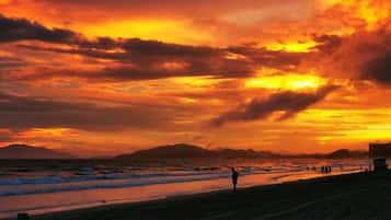 A beach scene with a sunset, silhouettes of people, and a distant mountain range.