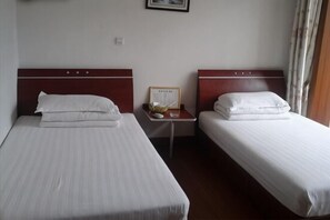 Two single beds with wooden headboards, a small table with a mirror and a framed picture, and a window with curtains. - Shanghai Xiangyi Hotel (Shanghai)